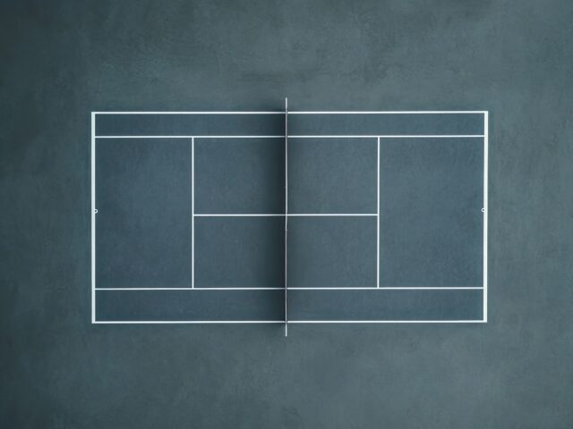 Close-up of a racquet or paddle sports court surface. The vibrant-colored tennis court features white boundary lines on a blue background, captured from a diagonal perspective